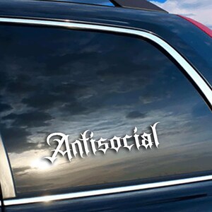 May include: White "Antisocial" decal in a gothic font, applied to a car window. The decal is centered on the window, with the sky and clouds reflected in the dark glass. The car is dark blue.