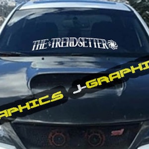 May include: A white car with a black hood and a windshield banner that reads "THE TRENDSETTER" with a stylized swirl design.