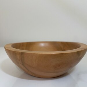 May include: A natural wood bowl with a light brown color and a smooth, rounded shape.