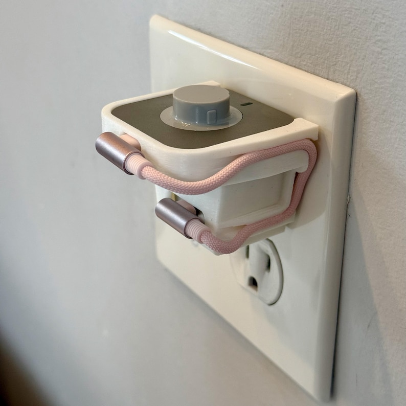 May include: A white and gray electrical outlet adapter with a gray dial and a pink braided charging cable. The adapter is plugged into a white wall outlet.