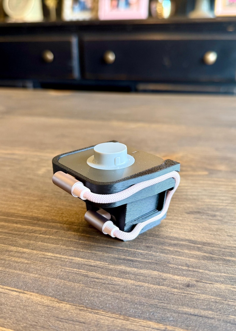 May include: A black and gray device with a white top and a pink and white cord. The device has two rose gold colored metal ends. The device is sitting on a wooden surface.