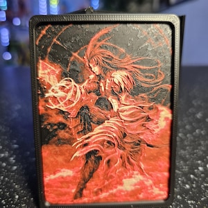 May include: A rectangular 3D printed plaque featuring a textured relief of a figure with long flowing hair, dressed in layered garments. The artwork uses a high-contrast color palette of deep black and vibrant red, set within a solid black frame.