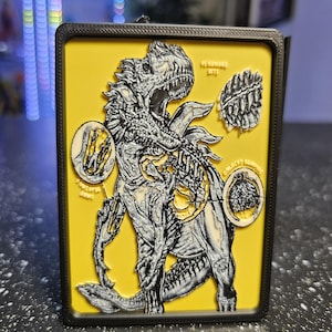 May include: A rectangular 3D-printed plaque with a black frame and a yellow background. It features a detailed black and white illustration of a dinosaur with anatomical callouts, including text labels like Venomous Bite, and two circular inset diagrams.