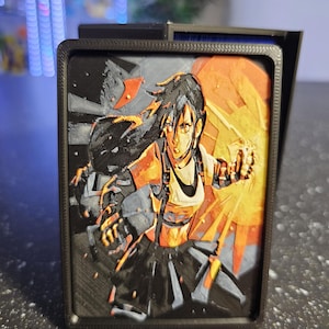May include: A black 3D-printed card holder featuring a detailed relief of a female anime character in a dynamic pose. The artwork is rendered in shades of black, orange, and gray, with a textured surface. The holder has a rectangular shape.