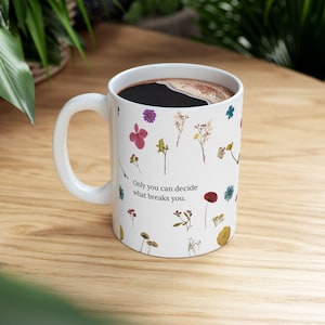 May include: White ceramic mug filled with dark liquid, featuring a floral design with various pressed flowers and the text: "Only you can decide what breaks you."