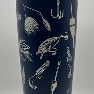 May include: Navy blue insulated tumbler with a silver rim and lid. The tumbler is decorated with a repeating pattern of fishing lures, hooks, and bobbers in a white, etched design. A great gift for anglers.