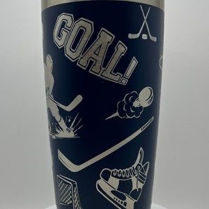 May include: A blue stainless steel tumbler with a silver lid. The tumbler is decorated with a hockey theme, including a hockey player, a hockey stick, a puck, and the word "GOAL!" in white lettering.