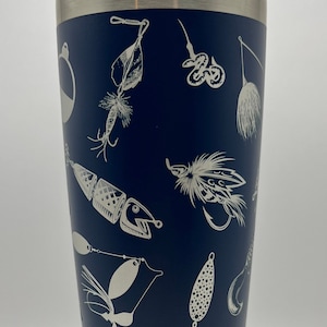 May include: Navy blue insulated tumbler with a silver rim and lid. The tumbler is decorated with a pattern of various fishing lures in a white, etched design. The tumbler is designed to keep beverages cold or hot.