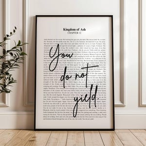 以下が含まれることがあります： 「Kingdom of Ash, Chapter 12」のテキストが印刷された黒いフレームのプリント。手書きの「You do not yield」という言葉が印刷されたテキストに重ねられています。プリントは白黒です。