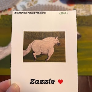 May include: A white horse runs through a green field. The image is printed on a white sticker with the text "Zazzle" and a red heart.