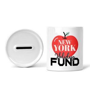 May include: White ceramic piggy bank with a red apple graphic and the text "New York Holiday Fund".
