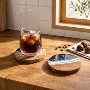 Può includere: Due sottobicchieri rotondi in legno con un design in resina blu e bianca, uno con un bicchiere di caffè freddo. I sottobicchieri hanno venature naturali del legno. Sono visibili anche chicchi di caffè e cioccolatini.