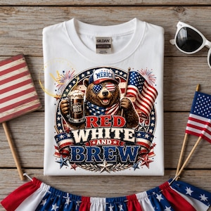 Könnte beinhalten: Ein weißes T-Shirt mit einer Grafik eines braunen Bären, der eine 'MERICA-Mütze und eine Flaggen-Sonnenbrille trägt und einen Krug mit der Aufschrift ROOT BEER hält. Das Design zeigt eine US-Flagge, Feuerwerk und den Text RED WHITE AND BREW.