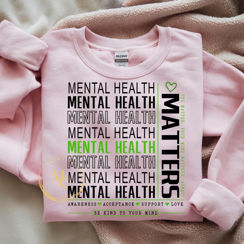 May include: A light pink sweatshirt with the words "MENTAL HEALTH" repeated in black and green. The word "MATTERS" is printed vertically in black and green. The bottom of the shirt reads "BE KIND TO YOUR MIND."