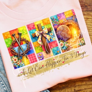 以下が含まれることがあります： 明るいピンク色のTシャツ。カラフルなグラフィックで宗教的なシンボルが描かれています。デザインには、リボン付きの十字架、釘、いばらの冠、空の墓が含まれています。「A Lot Can Happen In 3 Days」の文字が金色でプリントされています。