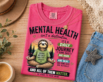 May include: A pink t-shirt featuring a graphic of a sloth sitting in a lotus position. The text reads: MENTAL HEALTH isn't a destination. IT'S A DAILY JOURNEY. SOME DAYS ARE HARD. SOME DAYS ARE OKAY. AND SOME DAYS ARE ACTUALLY AND ALL OF THEM MATTER.