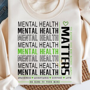 May include: Cream-colored sweatshirt with the words "MENTAL HEALTH" stacked vertically in black and green. The word "MATTERS" is printed vertically in green with the phrase "YOU MATTER, YOUR MIND MATTERS, ALWAYS". The bottom reads "BE KIND TO YOUR MIND".