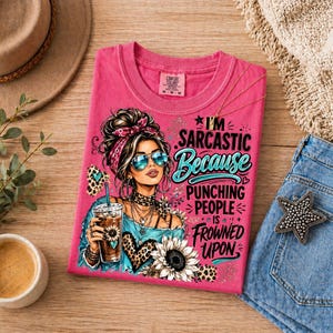 Pode incluir: Uma t-shirt rosa com o gr&aacute;fico de uma pessoa com fita na cabe&ccedil;a, &oacute;culos de sol e uma bebida. O texto diz: I'M SARCASTIC Because PUNCHING PEOPLE IS FROWNED UPON. O design inclui detalhes com estampa de leopardo e uma ilustra&ccedil;&atilde;o de girassol.