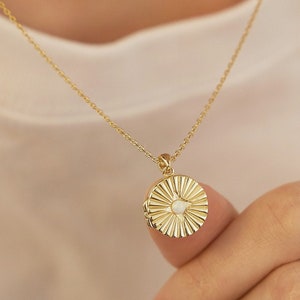 May include: A gold chain necklace with a round pendant featuring a sunburst design and a small white stone in the center.