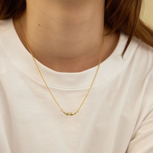 K&ouml;nnte beinhalten: Eine goldene Kettenkette mit einem kleinen, zarten Anh&auml;nger, der zwei ineinandergreifende H&auml;nde zeigt.