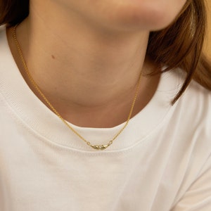 K&ouml;nnte beinhalten: Eine goldene Kettenkette mit einem kleinen, zarten Anh&auml;nger, der zwei ineinandergreifende H&auml;nde zeigt.