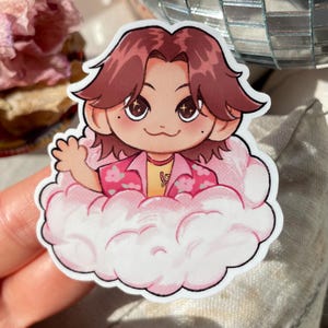 Peut inclure: Un autocollant de dessin animé d'une personne aux cheveux bruns portant une chemise à fleurs rose et blanche assise sur un nuage rose.