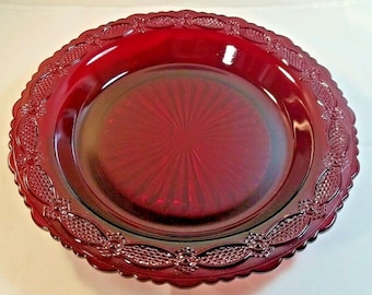 Peut inclure: Une assiette en verre rouge foncé avec un bord festonné et un motif décoratif autour du bord. L'assiette a un motif en étoile au centre.