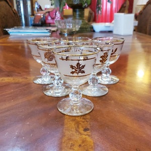 May include: Set of six clear glass stemmed drinking glasses with gold leaf accents. Each glass features a different leaf design.