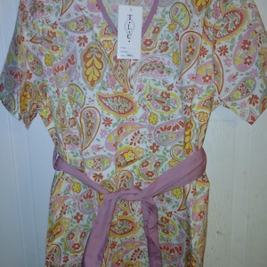 May include: A short-sleeved, V-neck top with a paisley pattern in shades of pink, yellow, and orange on a white background. It has a matching pink belt tied at the waist and a tag that says "T.L.C."