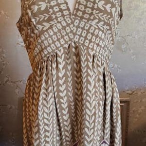 Puede incluir: Vestido sin mangas con cuello en V, con un estampado floral marr&oacute;n y blanco. El vestido tiene cintura fruncida y un borde floral morado en el dobladillo. El vestido se exhibe en un maniqu&iacute;.
