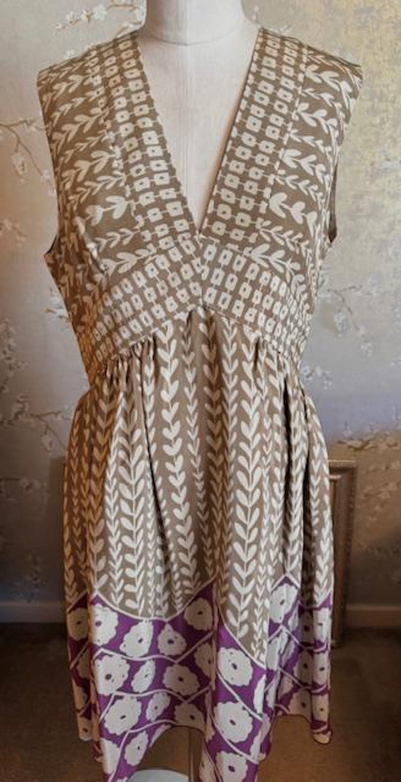 Puede incluir: Vestido sin mangas con cuello en V, con un estampado floral marr&oacute;n y blanco. El vestido tiene cintura fruncida y un borde floral morado en el dobladillo. El vestido se exhibe en un maniqu&iacute;.