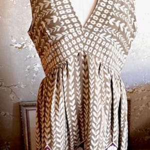 Puede incluir: Vestido sin mangas con cuello en V, exhibido en un maniqu&iacute;. El vestido presenta un patr&oacute;n geom&eacute;trico marr&oacute;n y blanco en el corpi&ntilde;o y un patr&oacute;n de hojas verticales en la falda. El dobladillo tiene un dise&ntilde;o floral morado y blanco.