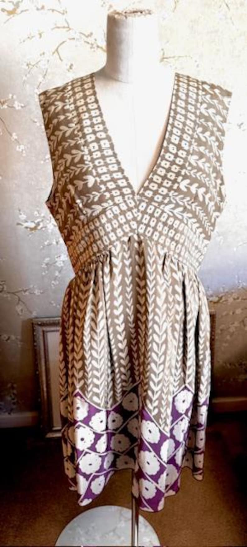 Puede incluir: Vestido sin mangas con cuello en V, exhibido en un maniqu&iacute;. El vestido presenta un patr&oacute;n geom&eacute;trico marr&oacute;n y blanco en el corpi&ntilde;o y un patr&oacute;n de hojas verticales en la falda. El dobladillo tiene un dise&ntilde;o floral morado y blanco.