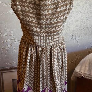 Puede incluir: Vestido sin mangas con un estampado de hojas marrones y blancas en el corpi&ntilde;o y la falda. La cintura est&aacute; ce&ntilde;ida con una banda de peque&ntilde;os cuadrados blancos. La parte inferior del vestido presenta un dise&ntilde;o floral morado y blanco.