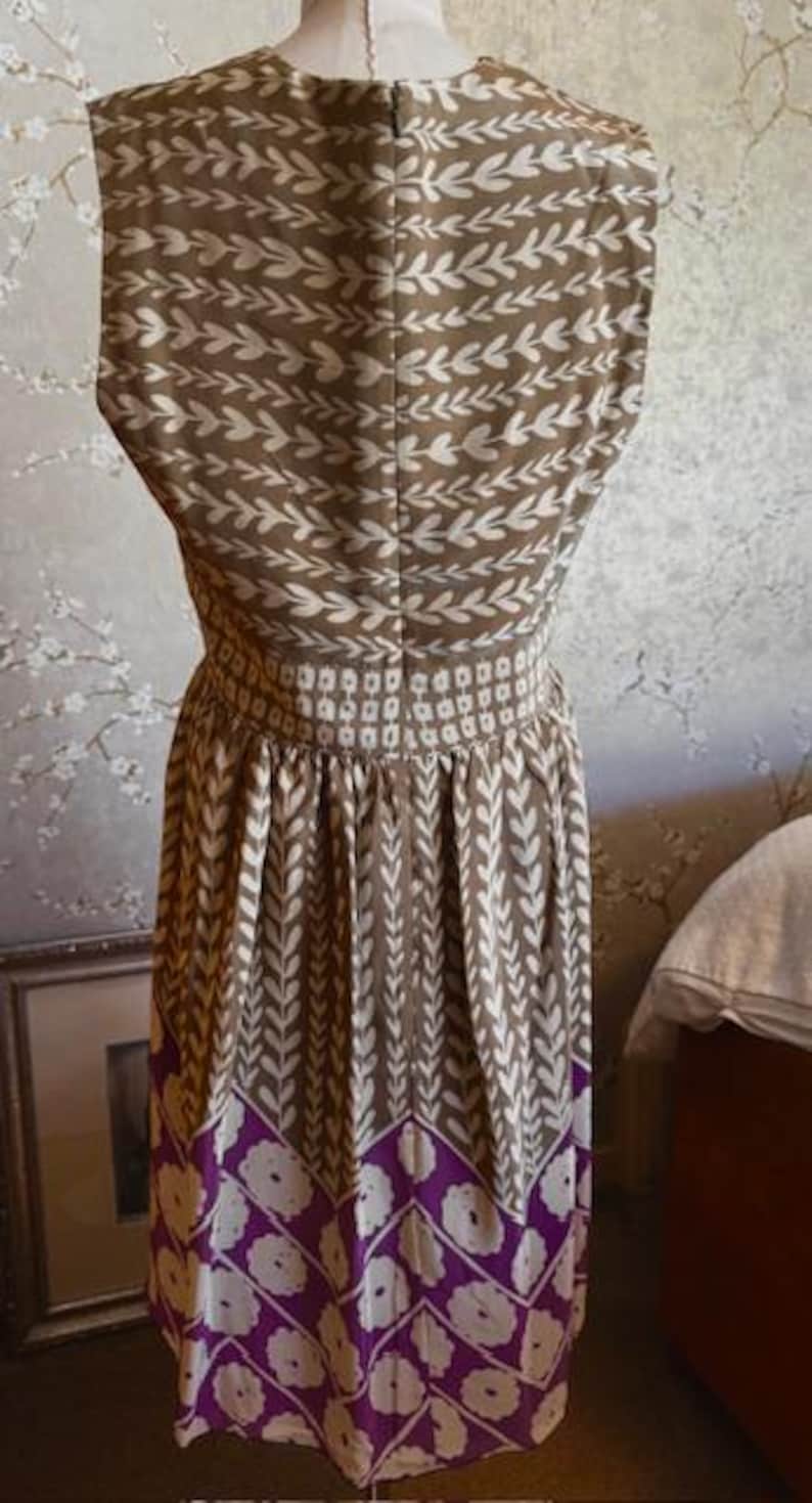 Puede incluir: Vestido sin mangas con un estampado de hojas marrones y blancas en el corpi&ntilde;o y la falda. La cintura est&aacute; ce&ntilde;ida con una banda de peque&ntilde;os cuadrados blancos. La parte inferior del vestido presenta un dise&ntilde;o floral morado y blanco.