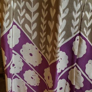 Puede incluir: Primer plano de una tela estampada, probablemente para ropa. El dise&ntilde;o se divide en secciones beige y moradas. Las secciones beige tienen un patr&oacute;n de hojas blancas, y las secciones moradas tienen un dise&ntilde;o floral blanco. La tela es probablemente para un vestido o prenda similar.