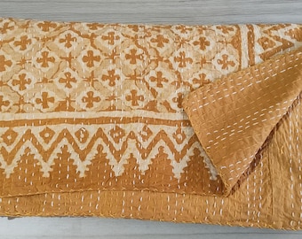 May include: A mustard yellow and cream cotton quilt featuring a repeating cross pattern and a geometric zigzag border. The textile is finished with visible white running stitch embroidery throughout, creating a textured, quilted appearance.