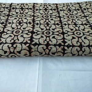 May include: A folded textile featuring a repeating pattern of beige floral motifs on a black background. The fabric is detailed with visible running stitches in white and red thread, creating a textured appearance across the entire surface.