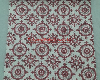 May include: A rolled-up white and burgundy quilt with a repeating floral pattern. The quilt features a border with a geometric design and the text "Triven fabricworld". The quilt is made of a soft, likely cotton, material.