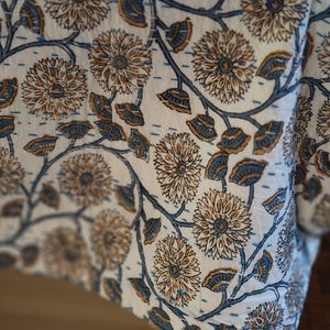 K&ouml;nnte beinhalten: Nahaufnahme eines wei&szlig;en Stoffes mit einem floralen Muster in Braun und Blau. Das Design zeigt gro&szlig;e Blumen und Bl&auml;tter, die durch Stiele verbunden sind. Der Stoff scheint eine Steppdecke oder ein &auml;hnliches Textil zu sein.