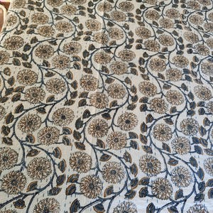 K&ouml;nnte beinhalten: Eine cremefarbene Blumensteppdecke mit einem sich wiederholenden Muster aus braunen und blauen Blumen und Ranken. Die Steppdecke hat ein durchgehendes Stichdesign, das Textur und Details hinzuf&uuml;gt. Das Gesamtdesign ist ein klassisches Blumenmuster.