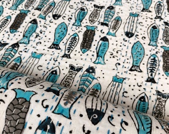 May include: White fabric with a repeating pattern of blue and grey fish. The fabric is folded in half, showing the pattern on both sides.
