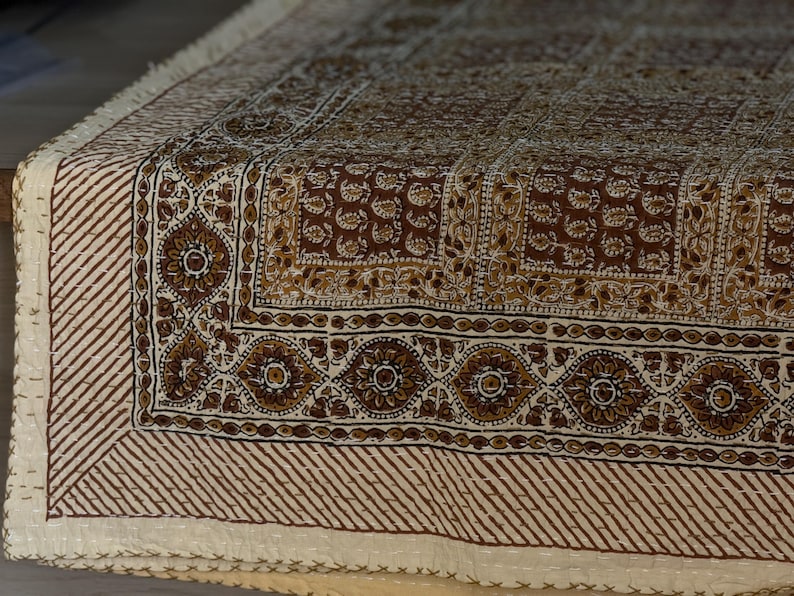 May include: A detailed close-up of a brown and cream-colored textile with an intricate floral and geometric pattern. The edges feature a striped design and fringe. The textile is likely a decorative item, such as a throw or tablecloth.