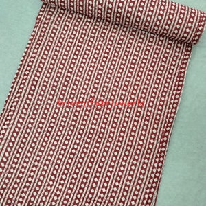 Könnte beinhalten: Ein roter und weißer Baumwollstoff mit einem Rautenmuster. Der Stoff ist aufgerollt und hat einen weißen Hintergrund mit roten Rauten.