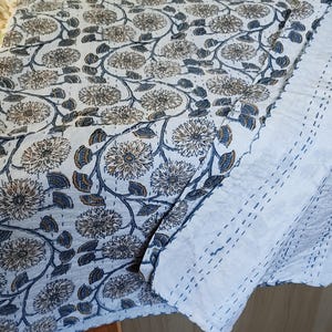 K&ouml;nnte beinhalten: Eine wei&szlig;e und blaue Steppdecke mit Blumenmuster. Die Steppdecke weist ein sich wiederholendes Muster aus gro&szlig;en, stilisierten Blumen und Bl&auml;ttern in Blau-, Braun- und Wei&szlig;t&ouml;nen auf. Die Steppdecke ist gefaltet und zeigt einen wei&szlig;en, gen&auml;hten Rand.