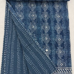 Pode incluir: Uma colcha kantha azul e branca com um padr&atilde;o geom&eacute;trico. A colcha est&aacute; dobrada ao meio e tem uma borda branca.