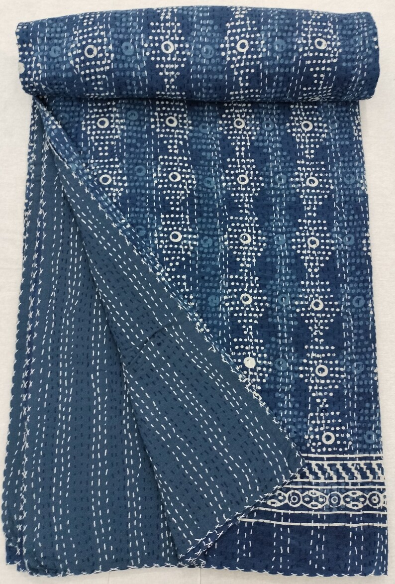 Pode incluir: Uma colcha kantha azul e branca com um padr&atilde;o geom&eacute;trico. A colcha est&aacute; dobrada ao meio e tem uma borda branca.
