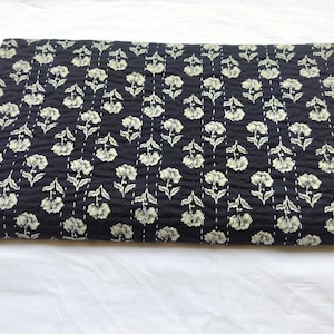 May include: A folded black fabric with a floral pattern in cream. The flowers are arranged in vertical rows and stitched with white thread. The fabric appears to be quilted, with a textured surface.