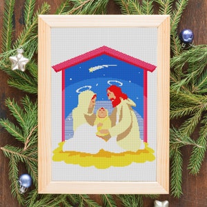 May include: A framed cross-stitch artwork depicting the nativity scene. The artwork features Mary, Joseph, and baby Jesus in a manger with a star above them. The background is a blue sky with stars and a shooting star.