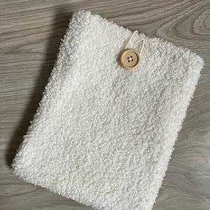 Può includere: Una pochette bianca e soffice con chiusura a bottone in legno. La pochette è realizzata in un materiale morbido e soffice.